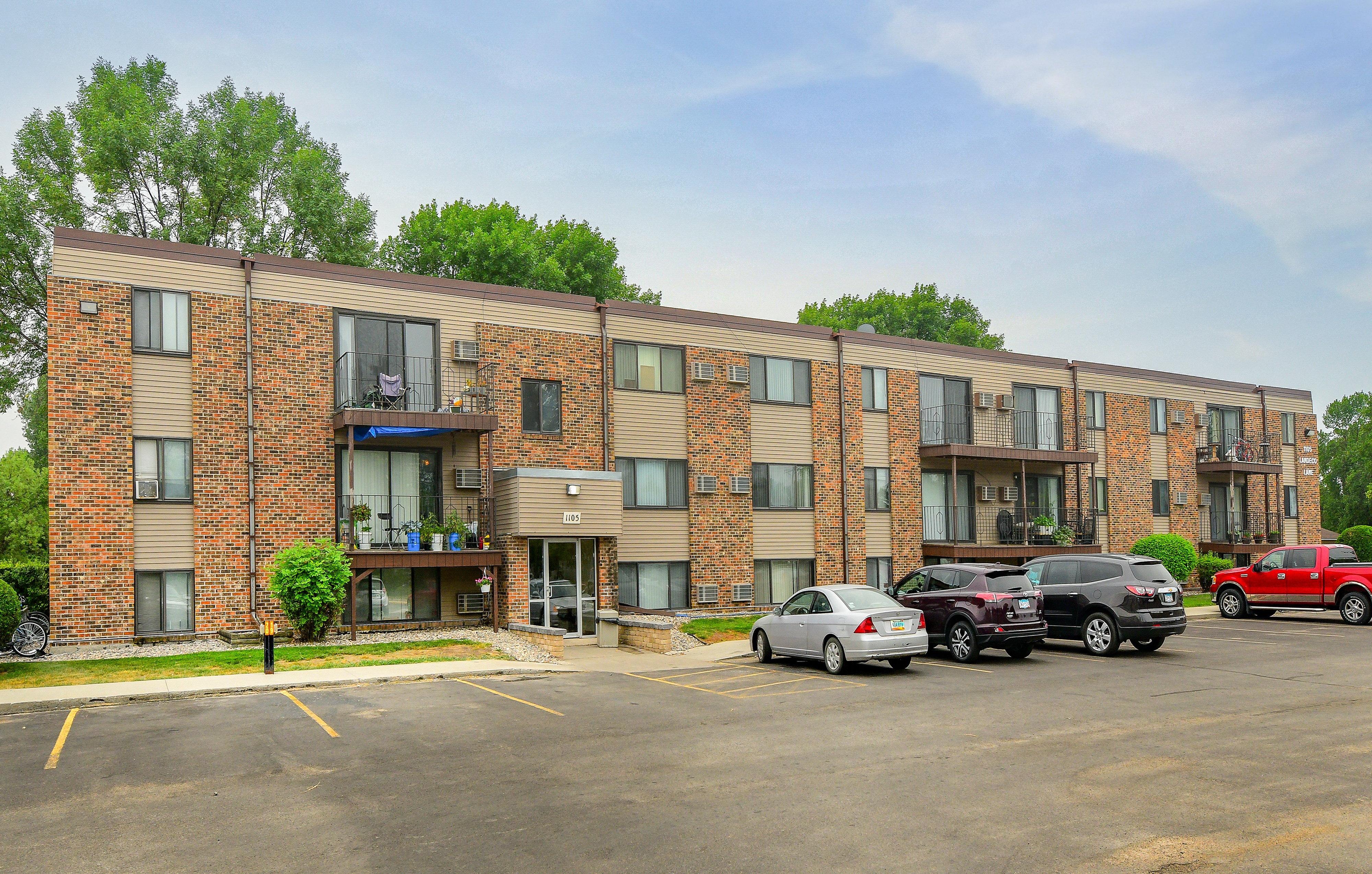 A parking lot in front of a brick apartment building with cars parked.